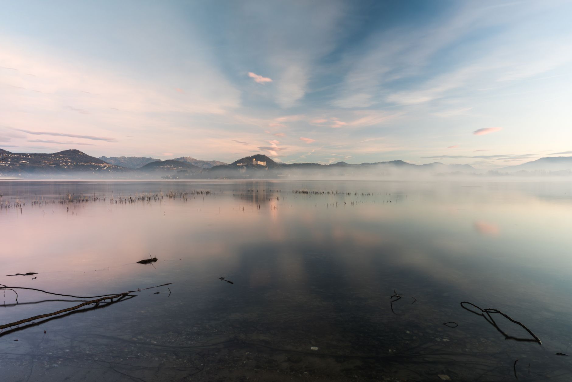 A misty lake reflecting the mountains at sunrise.